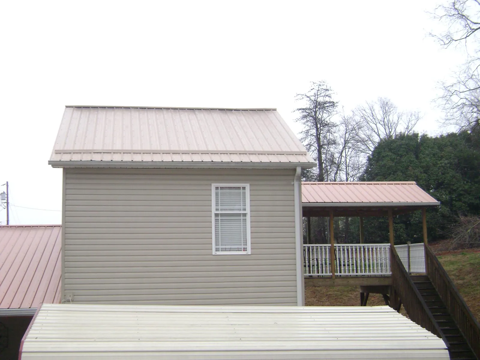 Tan metal roofs on a two story addition and attached porch, from a Roof Replacement job in Lexington